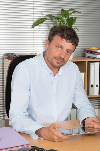 Geschäftsmann mit digitalem Tablet am Schreibtisch lächelt in die Kamera — Stockfoto