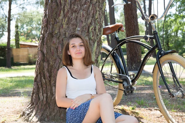 Jeune femme assise dans le parc alors que la bicyclette couchée au premier plan — Photo
