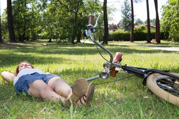 Молодая женщина с велосипедом лежит на траве в летнем парке — стоковое фото