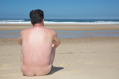 Çıplak adam boş bir kumsalda oturuyor ve meditasyon.