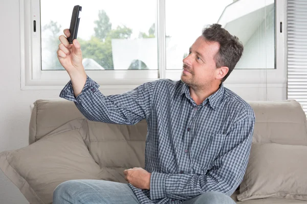 Hombre en casa sentado en el sofá y haciendo una selfie — Foto de Stock