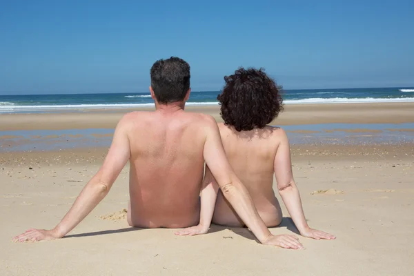 Coppia nudisti rilassanti seduti sulla spiaggia sotto il cielo blu profondo — Foto Stock