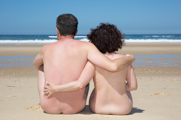 Naked couple sitting on the beach cuddling each other