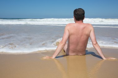 Adam çapraz bacaklı boş bir kumsalda oturuyor ve meditasyon.