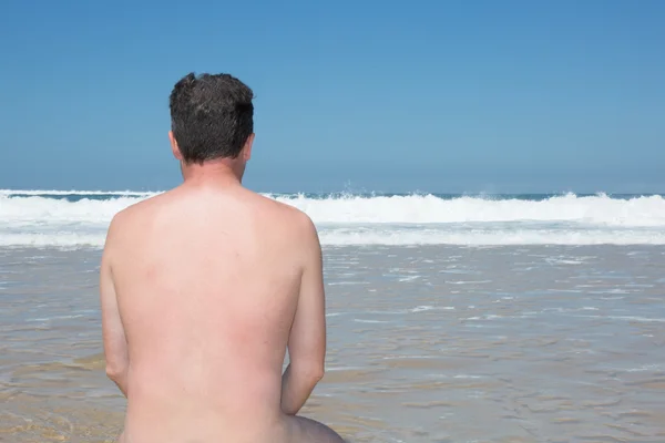 Homem nu está sentado de pernas cruzadas em uma praia vazia e meditando . — Fotografia de Stock