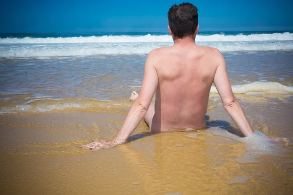 Homem nu está sentado de pernas cruzadas em uma praia vazia e meditando . — Fotografia de Stock