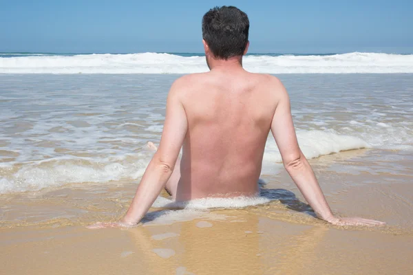 O homem relaxante está sentado de pernas cruzadas em uma praia vazia e meditando . — Fotografia de Stock