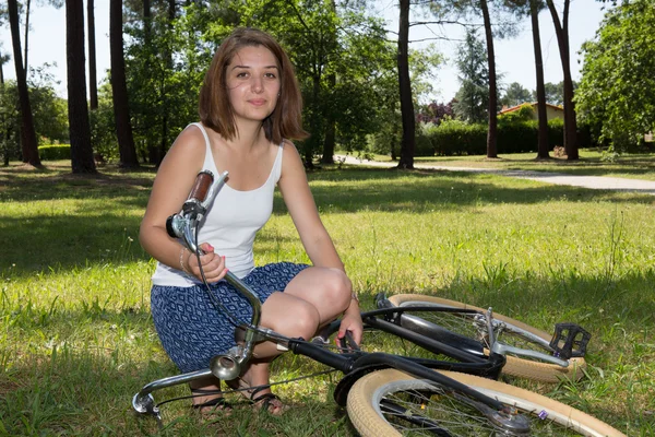 Красивая улыбающаяся девушка, сидящая рядом с велосипедом — стоковое фото