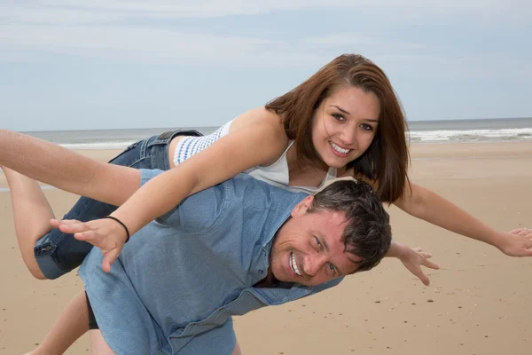 背着夫妇拥抱和欢笑在海滩上 — 图库照片