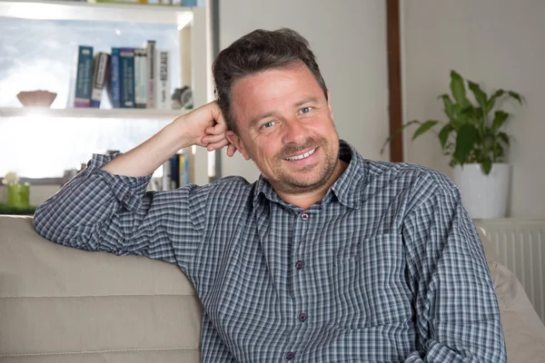 Mature smiling man sitting in couch at home — Stock Photo, Image