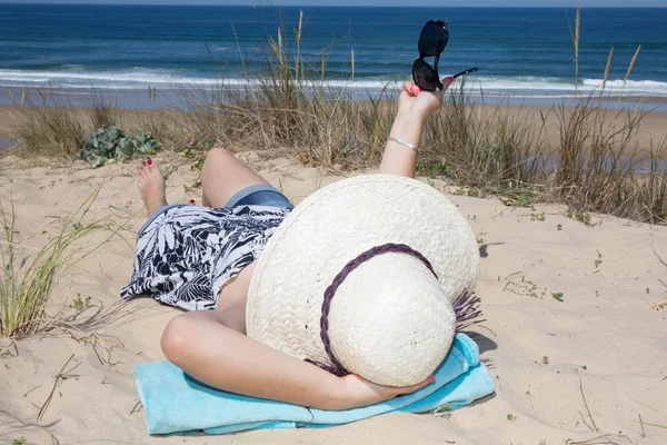 Foto en la playa de una mujer acostada en el sombrero — Foto de Stock