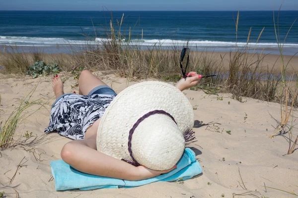 Foto en la playa de una mujer acostada en el sombrero — Foto de Stock