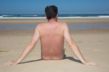 Çıplak bir adam bir boş plaj rahatlatıcı oturuyor