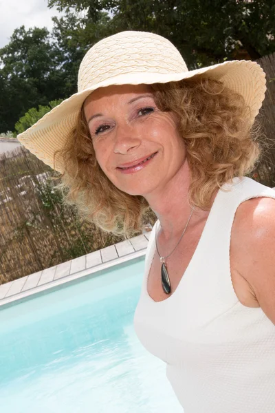 Elegant blonde with hat and white dress to the pool