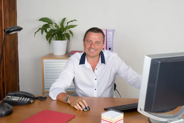 Geschäftsmann, der im Büro arbeitet, am Schreibtisch sitzt, auf den Computerbildschirm blickt, lächelt — Stockfoto