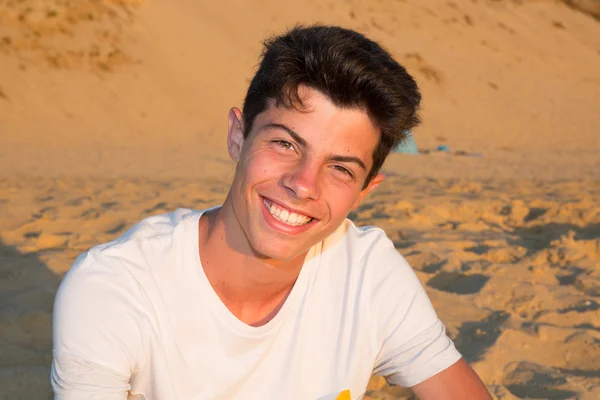 Bello giovane sulla spiaggia sorridente alla macchina fotografica — Foto Stock