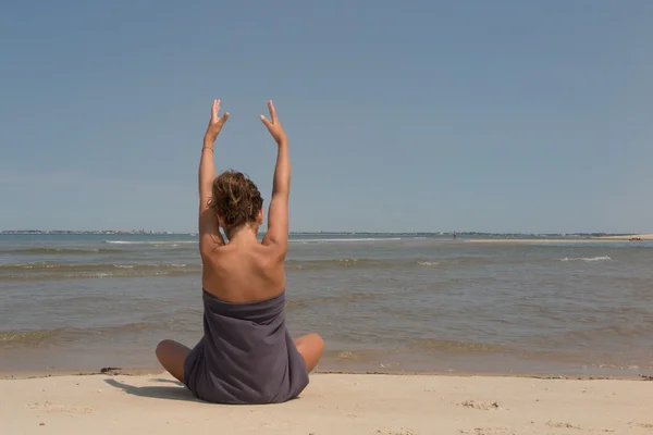 Porträtt av en vacker ung kvinna som sitter i yogaställning på stranden — Stockfoto