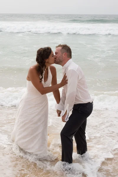 Recién casados compartiendo un momento romántico en la playa besándose — Foto de Stock