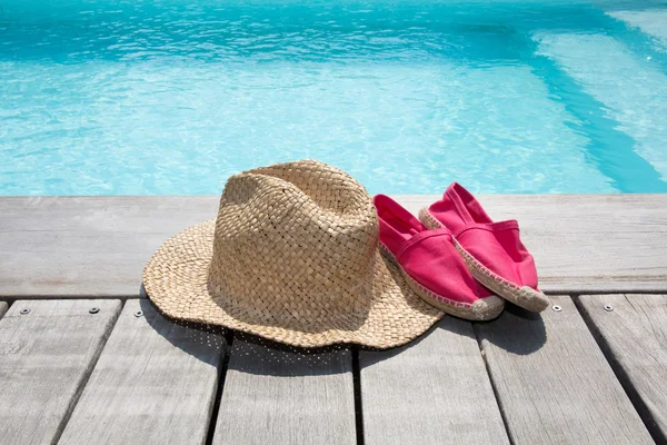 Fondo de verano con zapatos de sombrero en la cubierta de madera y la piscina — Foto de Stock