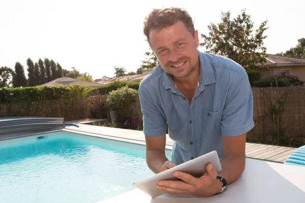 Hombre casual de pie junto a la piscina sonriendo con la tableta digital — Foto de Stock