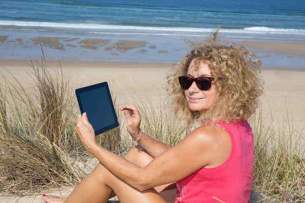 Mujer rubia usando tableta electrónica en la playa — Foto de Stock