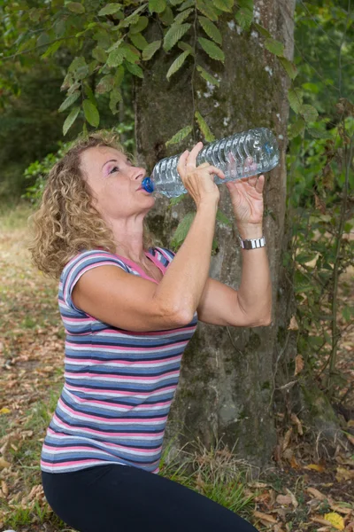 Portrait d'une femme blonde buvant de l'eau au parc vert d'été . — Photo