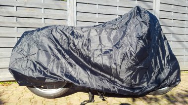 Motosiklet, gümüş ve mavi motosikletle korunuyor. Motosikletin üzerinde branda kaplama var.
