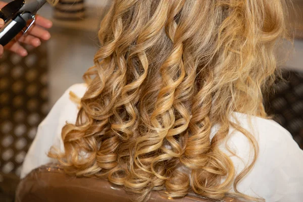 Young woman blond curly getting beautiful hairstyle in hair salon hairdresser