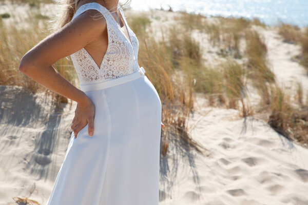 beautiful pregnant bride with her wedding dress at dune sand beach
