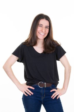 Uzun kahverengi saçlı, mutlu esmer kadın gülümsüyor ve elleri kot pantolonun cebinde duruyor.