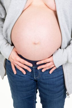 Açık gri yelek ve kot pantolon giymiş hamile bir kadının karnı.