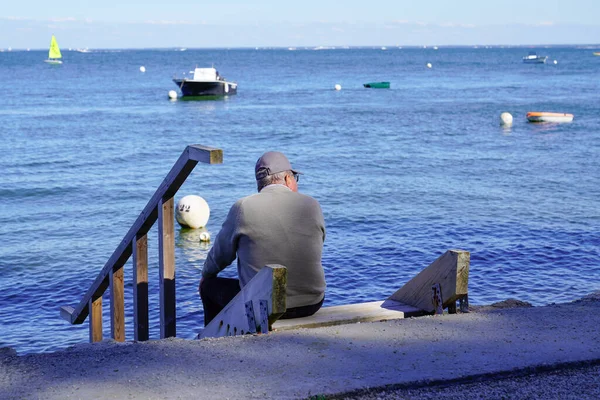 上了年纪的老人坐在木制楼梯上 在涨潮时眺望着大海的海滨 — 图库照片