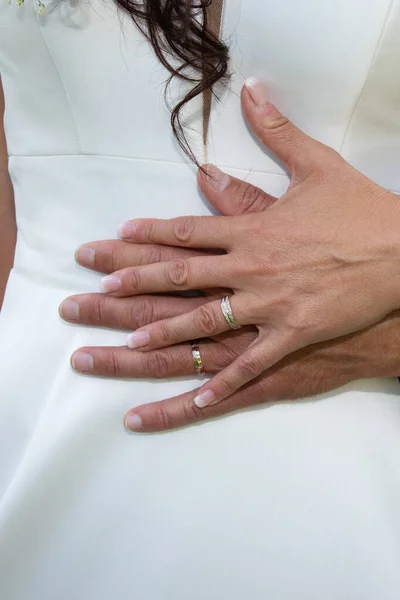wedding finger rings on bride groom hands on white dress background