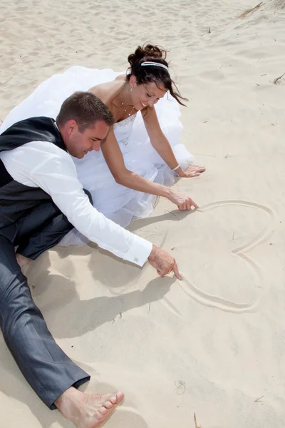 De & bruidegom bruid getrouwd paar tekening een hart op een strand — Stockfoto