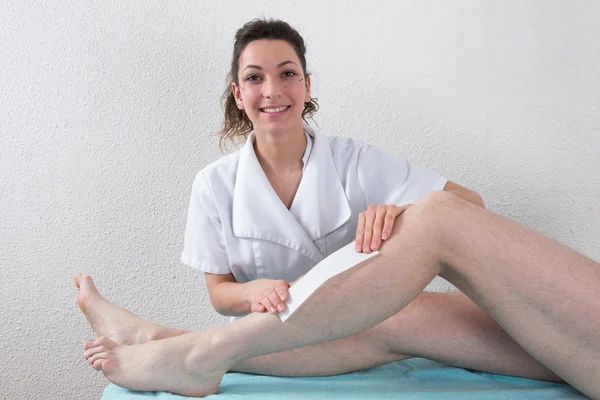 A beautician waxing a man's leg applying wax strip — Stock Photo, Image