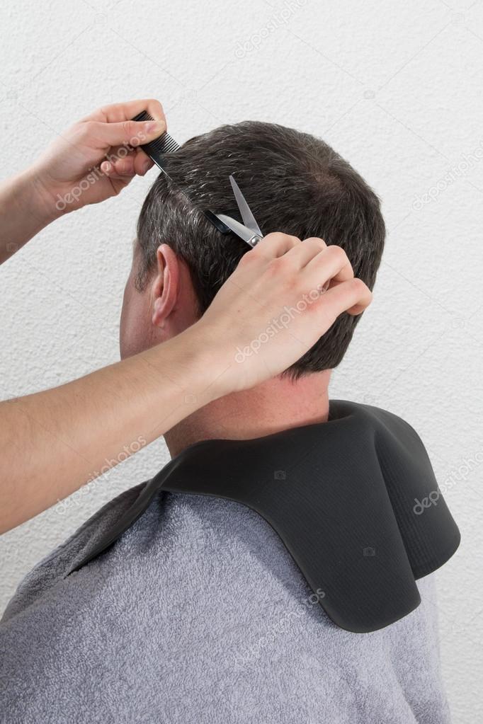 Hairdresser trimming man's brown hair with scissors