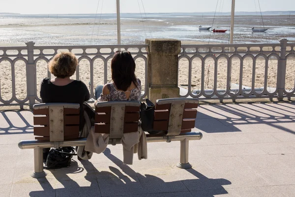 Una vista posteriore di persone sedute su una panchina sul lato mare — Foto Stock