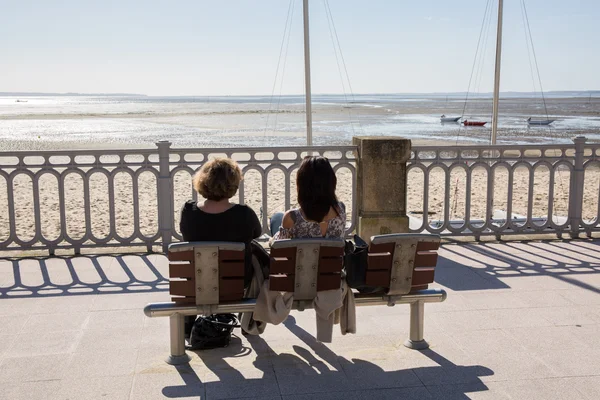 Una vista trasera de las personas sentadas en un banco junto al mar — Foto de Stock