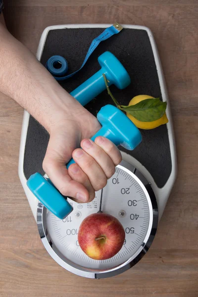 Fresh apple and dumbbells tied with a measuring tape on a weighting scale — Stock Photo, Image
