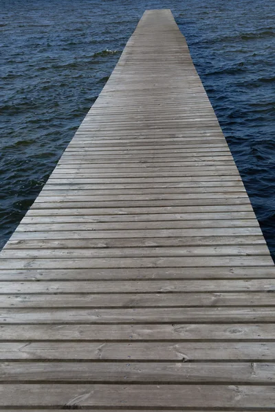 Viejo pontón de madera que conduce al horizonte sobre el agua por el día azul — Foto de Stock