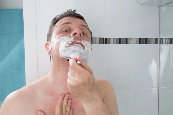 Man scheren met een scheermesje en scheerschuim in badkamer — Stockfoto