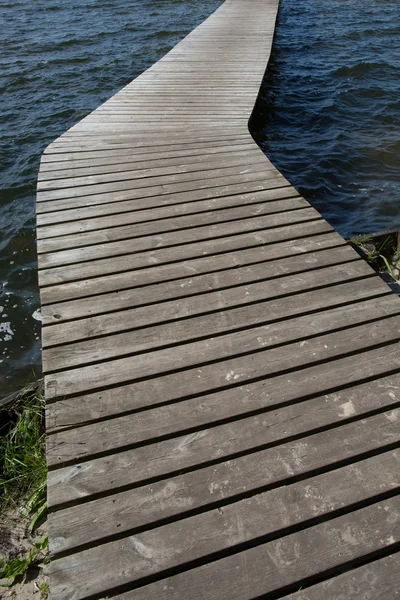 Viejo pontón de madera que conduce al horizonte sobre el agua por el día azul — Foto de Stock