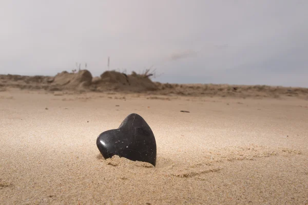 Black zen stone in shape of heart, on sand background — Stock Photo, Image