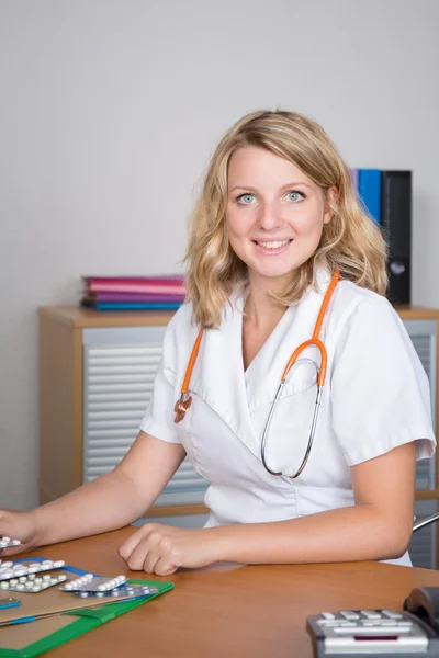 Attraktive blonde Ärztin mit Pillen auf dem Schreibtisch — Stockfoto