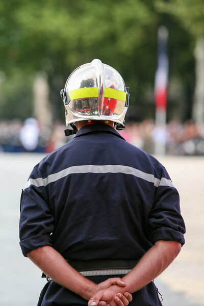 firefighter seen from behind hands crossed supervising an intervention in official french uniform with fireman helmet