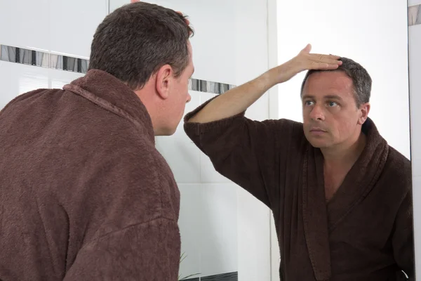 Человек перед зеркалом смотрит на свои волосы — стоковое фото