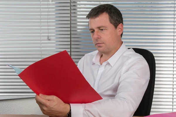 Man zit in zijn kantoorruimte terwijl serieus kijken naar zijn map — Stockfoto