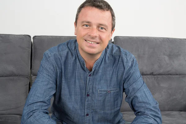 Hombre guapo y sonriente sentado en el sofá en casa — Foto de Stock