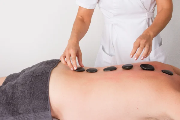 Hombre adulto recibiendo un masaje de piedra caliente acostado . — Foto de Stock