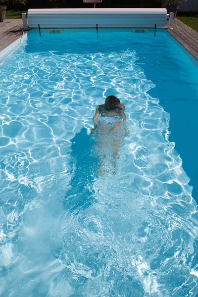 Mujer con traje de baño nadando en una piscina de agua azul — Foto de Stock